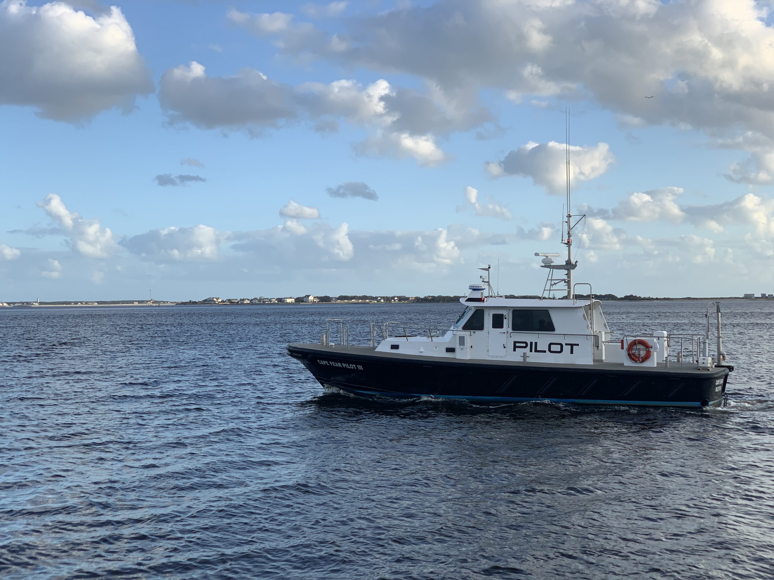 light blue sky with grey clouds over mostly calm waters with a black and white boat with "pilot" written in black on the side