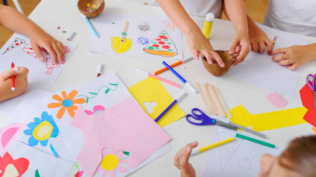table covered in craft materials like scissors and construction paper with small hands reaching in